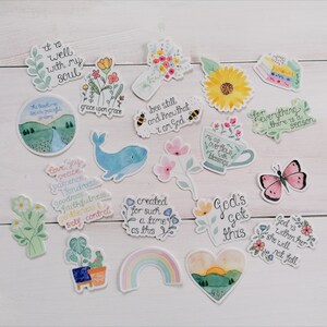 May include: A collection of 15 watercolor stickers with inspirational quotes and illustrations. The stickers feature a variety of designs, including flowers, butterflies, rainbows, and a whale. The quotes include "It is well with my soul", "Grace upon grace", "Bee still and know that I am God", "For everything there is a season", "God's got this", and "God is within her, she will not fall".