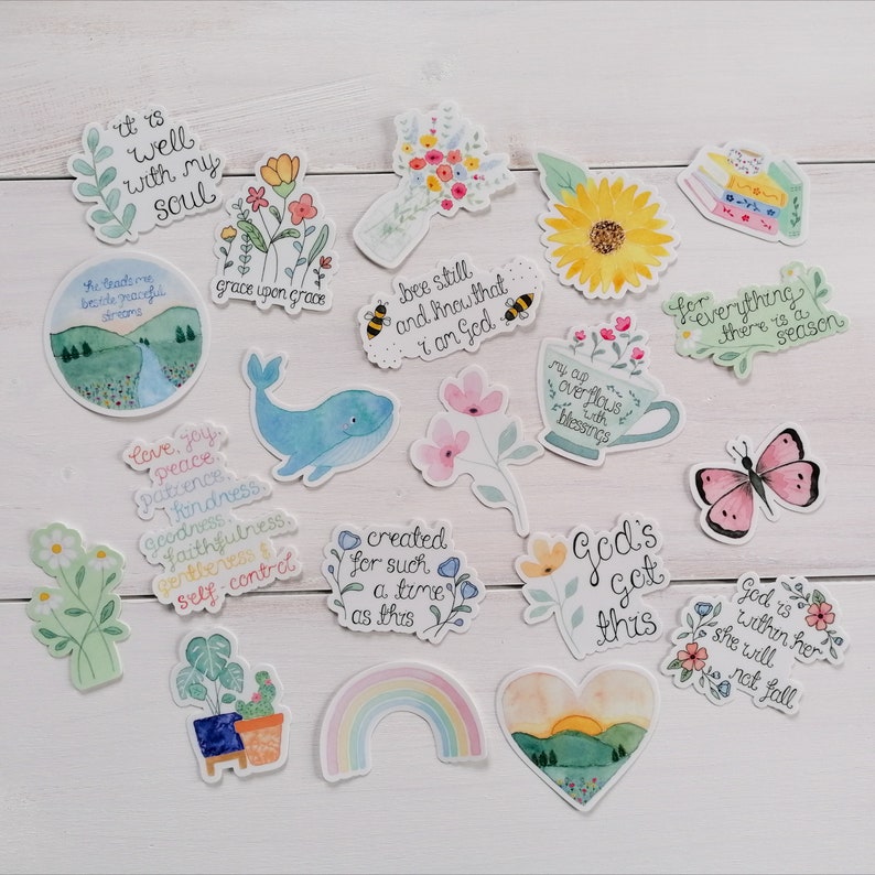 May include: A collection of 15 watercolor stickers with inspirational quotes and illustrations. The stickers feature a variety of designs, including flowers, butterflies, rainbows, and a whale. The quotes include "It is well with my soul", "Grace upon grace", "Bee still and know that I am God", "For everything there is a season", "God's got this", and "God is within her, she will not fall".