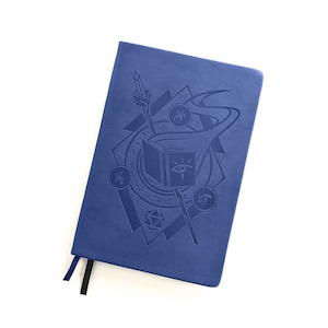 May include: A blue notebook with an embossed design featuring a book, a staff, and a dice. The design is in a geometric pattern with runes and symbols.