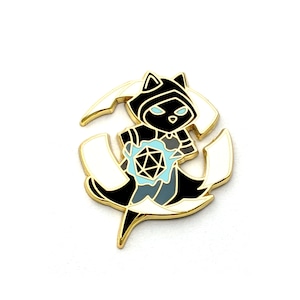 May include: A gold-colored enamel pin featuring a black cat wearing a hooded robe and holding a blue and black dice. The cat is surrounded by two white crescent moons.