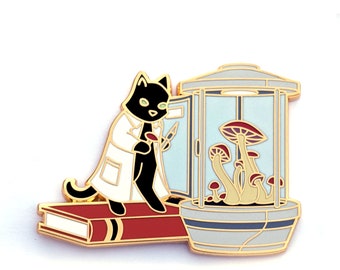 May include: A black cat wearing a white lab coat holds a small red mushroom in a glass terrarium with other mushrooms growing inside. The terrarium is on a red book with a gold spine.