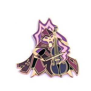 May include: A gold-colored enamel pin featuring a character in a purple and black hooded cloak playing a cello. The character has a mask and is surrounded by a stylized, wavy design in shades of pink and purple.