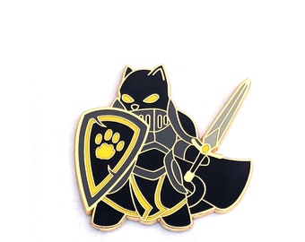 May include: A black and gold enamel pin featuring a cat warrior with a shield and sword. The shield has a yellow paw print. The cat is wearing armor and a cape. The pin has a gold border and is set against a white background.