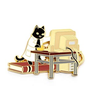 May include: Gold enamel pin depicting a black cat wearing a white lab coat and sitting on a book, using a computer. The cat is holding a yellow rubber ducky.