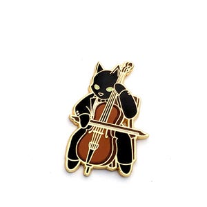 May include: Gold-tone enamel pin depicting a black cat playing a cello. The cat is wearing a tuxedo and has green eyes. The cello is brown and has a gold-tone string.