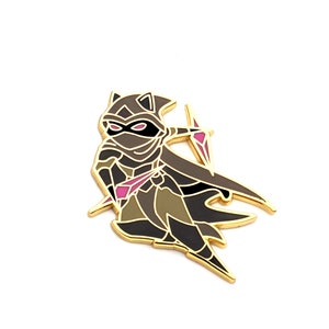 May include: Gold-tone enamel pin featuring a cartoon character wearing a black hooded cloak and mask, holding a pink and purple dagger. The character has cat ears and is in a fighting pose.