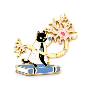 May include: Gold-tone enamel pin featuring a black cat wearing a white lab coat and holding a pink and yellow neuron. The cat is standing on a blue book with gold accents.