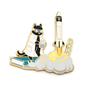 May include: A black cat wearing a white lab coat and goggles stands on a book holding a cube. A rocket ship with a white body and orange flames launches into the air behind the cat.