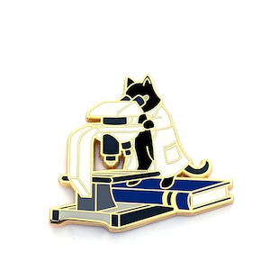 May include: A black cat wearing a white lab coat looks through a microscope. The microscope is sitting on a blue book with a gold base.