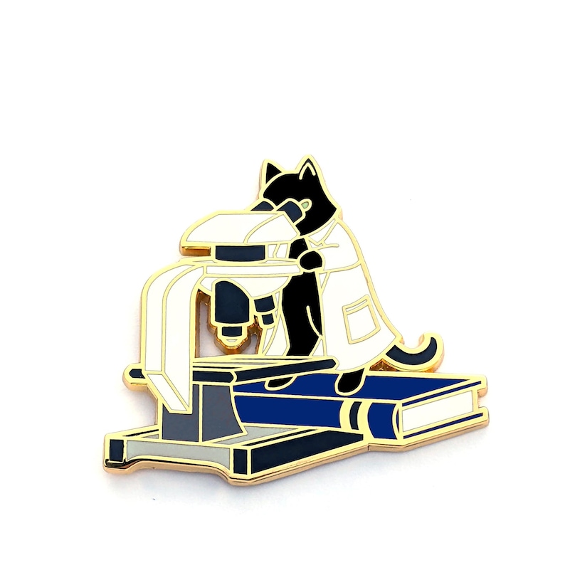 May include: A black cat wearing a white lab coat looks through a microscope. The microscope is sitting on a blue book with a gold base.