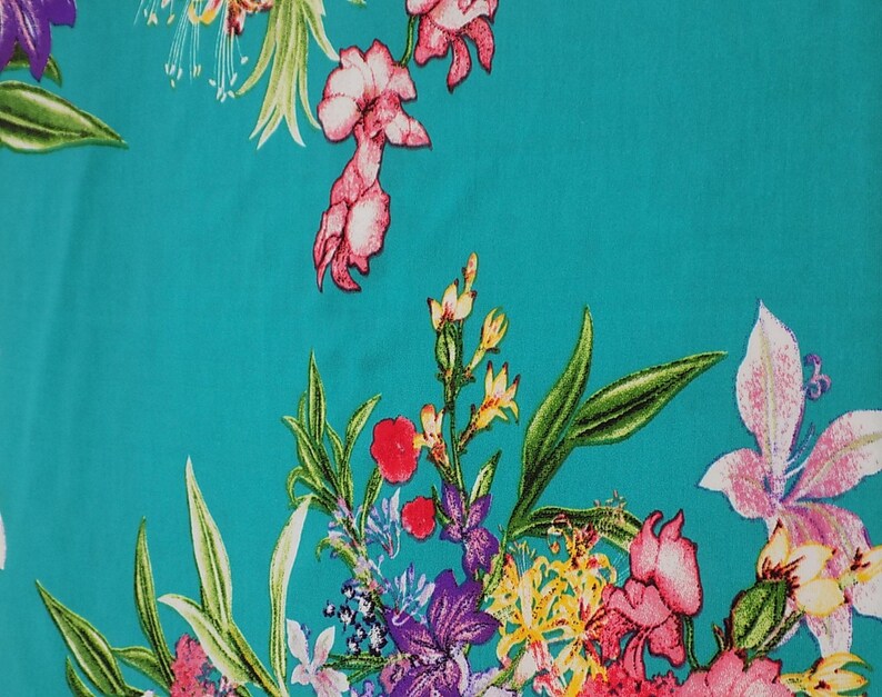 May include: A vibrant turquoise fabric featuring a floral pattern. The design includes various flowers in shades of pink, purple, red, and yellow, with green leaves. The flowers are scattered across the fabric.