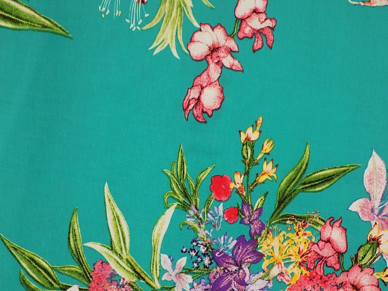May include: A vibrant teal fabric featuring a floral pattern. The design includes pink, red, yellow, and purple flowers with green leaves. The flowers are scattered across the fabric, creating a lively and colorful design.