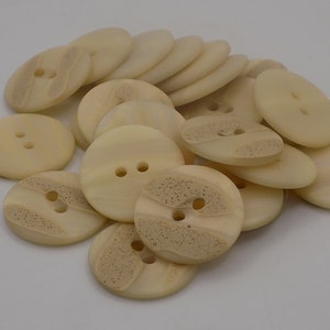 Peut inclure: Un tas de boutons de couleur crème avec deux trous chacun. Certains boutons ont un design texturé.