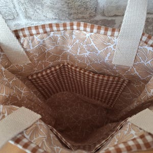 Peut inclure: Un sac fourre-tout brun et blanc avec un motif vichy et un imprim&eacute; floral. Le sac a une grande poche &agrave; l'int&eacute;rieur.