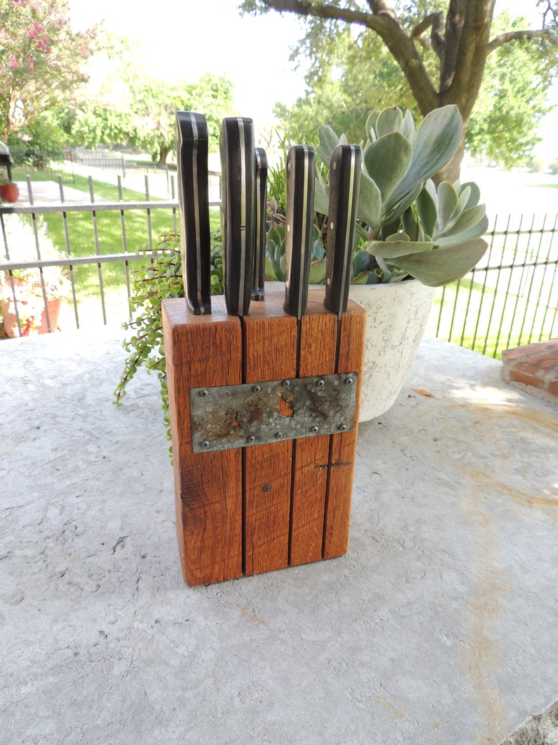 Puede incluir: Un bloque de cuchillos de madera con un acento met&aacute;lico, que contiene cinco cuchillos con mangos negros. El bloque est&aacute; hecho de madera recuperada y tiene un aspecto r&uacute;stico.