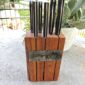 Puede incluir: Un bloque de cuchillos de madera con una placa de metal en la parte delantera. El bloque est&aacute; lleno de seis cuchillos con mangos negros y plateados.