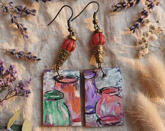 May include: A pair of rectangular dangle earrings featuring hand-painted illustrations of colorful vases in shades of green, orange, purple, and pink. The earrings are suspended from bronze-toned metal hooks with a small orange bead and a textured cone.