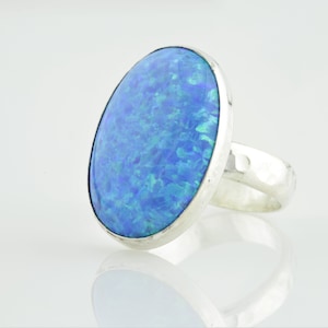 May include: A silver ring featuring a large oval blue opal gemstone. The ring has a hammered band.