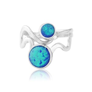 Pode incluir: Um anel de prata com duas pedras de opala azul engastadas em um design ondulado.