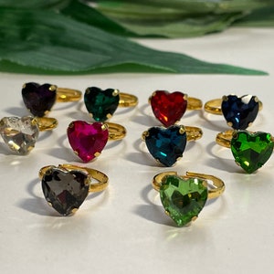 May include: Assortment of ten gold heart-shaped rings with colourful rhinestones. The rings feature a variety of colours including red, green, blue, black, and clear.