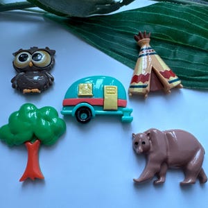 May include: A set of five colorful resin figurines depicting a camper, a tree, an owl, a bear, and a teepee. The figurines are all in a camping theme.
