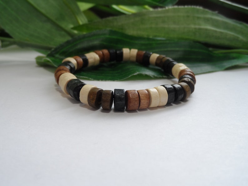 May include: A wooden bracelet with brown, black, and white beads. The bracelet is made of natural wood and has a simple, elegant design.