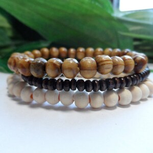 May include: Three wooden bead bracelets in brown, light brown, and white. The bracelets are stacked on top of each other.