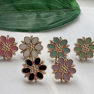 May include: Six flower-shaped metal buttons in various colours, including pink, white, light blue, green, black, and purple.