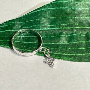 May include: A silver ring with a small silver charm shaped like the letter "H" hanging from it. The ring is on a green background.
