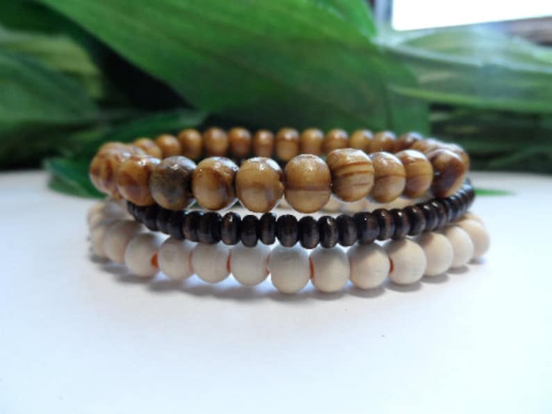 May include: Three wooden bead bracelets in brown, light brown, and white. The bracelets are stacked on top of each other.
