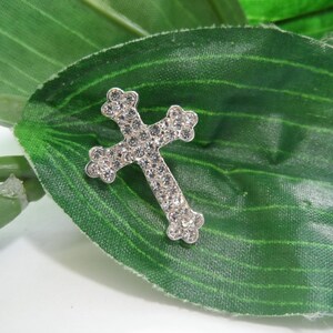 May include: A silver cross with clear rhinestones on a green leaf background.