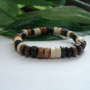 May include: A wooden bracelet with brown, black, and white beads. The bracelet is made of round beads that are strung together.