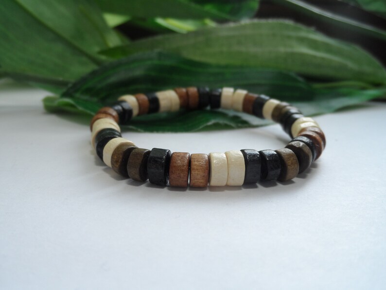 May include: A wooden bracelet with brown, black, and white beads. The bracelet is made of round beads that are strung together.