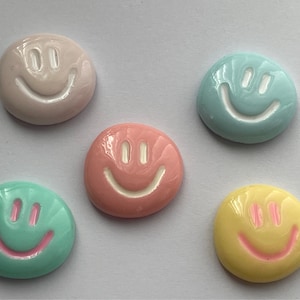 May include: Five smiley face buttons in different pastel colors. The buttons are round and have a white smiley face design. The colors are pink, light blue, yellow, green, and a darker shade of blue.