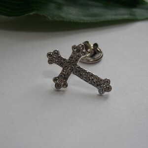 May include: A silver cross charm with clear rhinestones. The cross is attached to a metal ring.