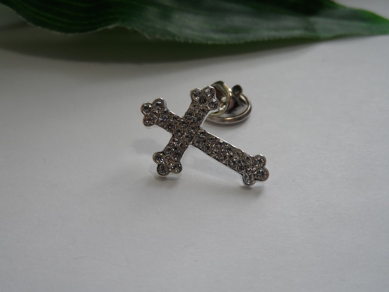 May include: A silver cross charm with clear rhinestones. The cross is attached to a metal ring.