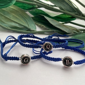 May include: Three blue friendship bracelets with silver charms featuring typewriter keys with the letters Q, G, and B.