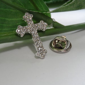 May include: A silver cross pin with clear rhinestones. The pin has a safety clasp on the back.