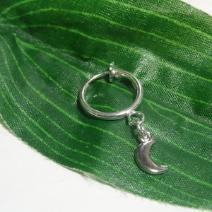 May include: Silver crescent moon charm dangling from a silver hoop earring. The earring is a clip-on style.