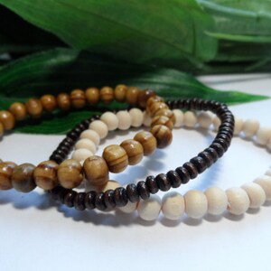 May include: Three wooden bead bracelets in brown, light brown, and white. The bracelets are stacked on top of each other.