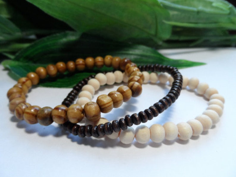 May include: Three wooden bead bracelets in brown, light brown, and white. The bracelets are stacked on top of each other.