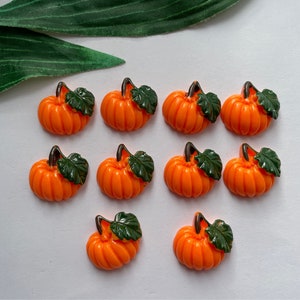 May include: Ten orange pumpkin-shaped buttons with green leaves. The buttons are about 1 inch in diameter and have a flat back.