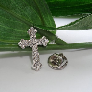 May include: Silver-toned cross pin with clear rhinestones. The pin has a safety clasp on the back.