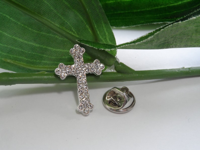 May include: Silver-toned cross pin with clear rhinestones. The pin has a safety clasp on the back.