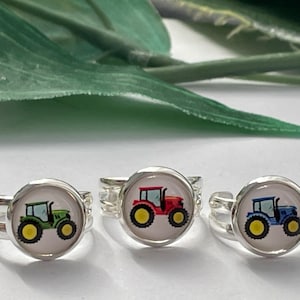 May include: Three silver rings with colorful tractor designs. The tractors are green, red, and blue.