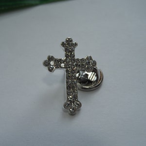 May include: A silver cross pin with clear rhinestones. The pin has a safety clasp on the back.