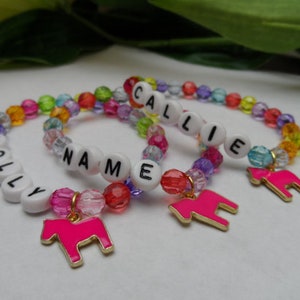 May include: Three colourful beaded bracelets with white letter beads spelling out the names "HOLLY", "NAME", and "CALLIE". Each bracelet has a pink horse charm.