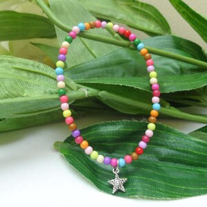 May include: A colourful beaded bracelet with a star charm. The bracelet is made of small, round beads in various colours, including pink, blue, green, yellow, and orange. The star charm is silver and has a five-pointed star design.