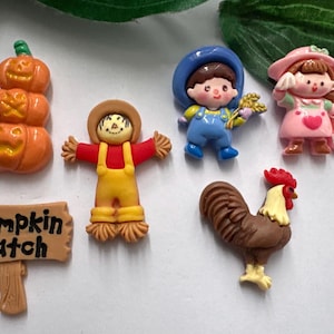 Op de afbeelding: Een verzameling kleurrijke decoratieve beeldjes met herfstthema. Inclusief een stapel oranje pompoenen, een vogelverschrikker, een jongen in een blauwe overall, een meisje in een roze jurk, een haan en een bord met "Pumpkin Patch".