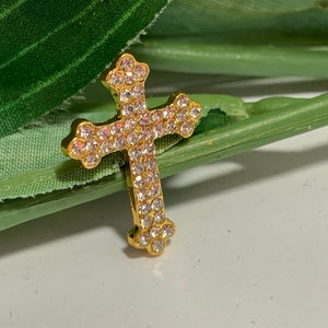 May include: A gold-toned cross pendant encrusted with clear rhinestones.
